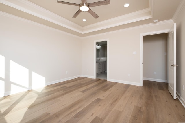 unfurnished bedroom featuring ensuite bathroom, ornamental molding, a tray ceiling, ceiling fan, and light hardwood / wood-style floors