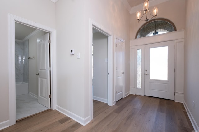 entryway with ornamental molding, a towering ceiling, a chandelier, and light wood-type flooring