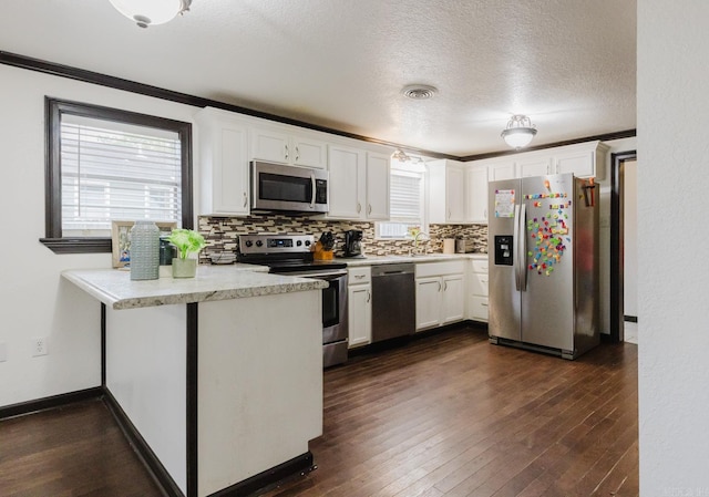 kitchen featuring white cabinetry, appliances with stainless steel finishes, a textured ceiling, dark wood-type flooring, and kitchen peninsula