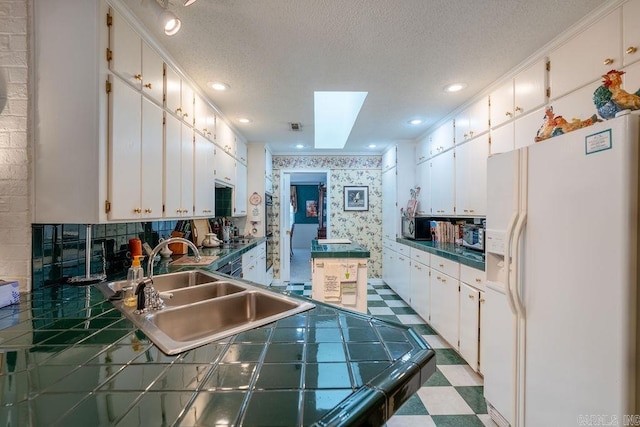 kitchen featuring white refrigerator with ice dispenser, a textured ceiling, white cabinets, and tile counters