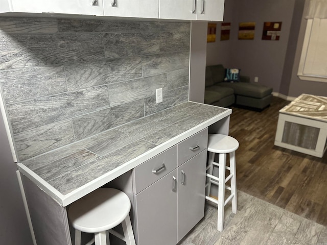 kitchen with a kitchen bar, gray cabinets, dark hardwood / wood-style floors, and backsplash