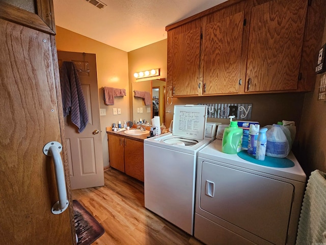 laundry room featuring a textured ceiling, light hardwood / wood-style flooring, washer and clothes dryer, and sink