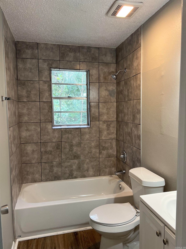 full bathroom with hardwood / wood-style floors, a textured ceiling, tiled shower / bath, and vanity