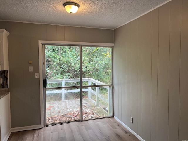 doorway featuring wood walls, a textured ceiling, and light hardwood / wood-style floors