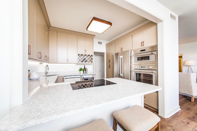 kitchen featuring a peninsula, a sink, stainless steel appliances, and cream cabinetry