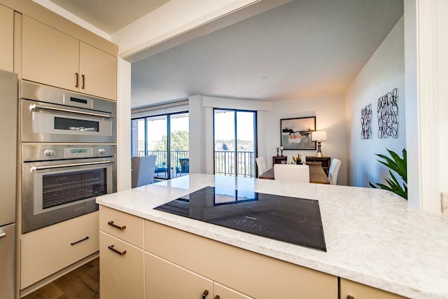 kitchen with cream cabinets, stainless steel double oven, black electric cooktop, open floor plan, and dark wood finished floors