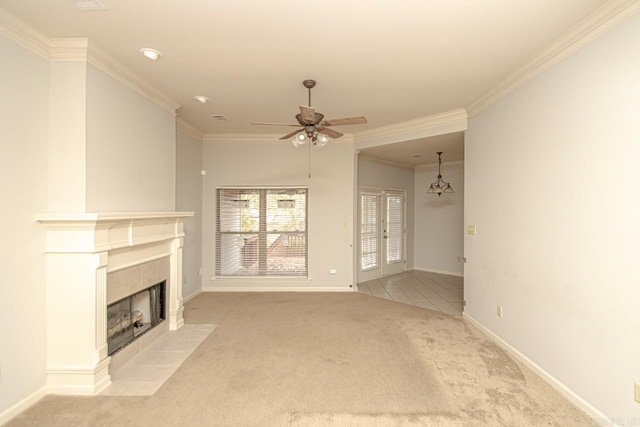 unfurnished living room featuring a tiled fireplace, ceiling fan with notable chandelier, light colored carpet, and crown molding