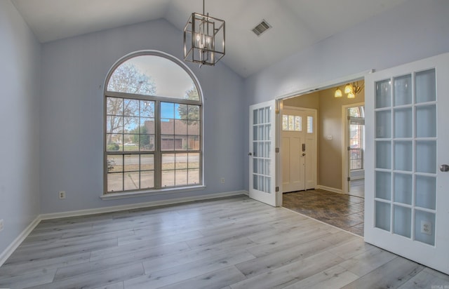 entryway featuring french doors, light wood-type flooring, lofted ceiling, and a chandelier