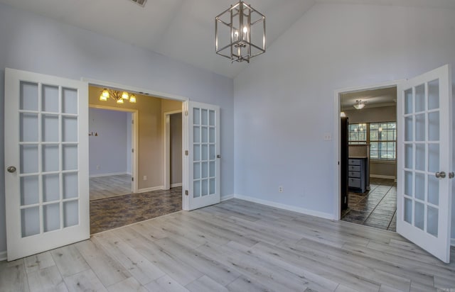 spare room with high vaulted ceiling, light wood-type flooring, a chandelier, and french doors