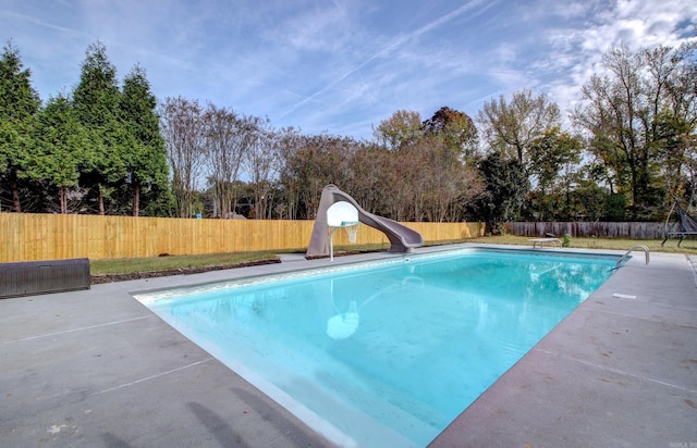 view of swimming pool with a water slide, a diving board, and a patio