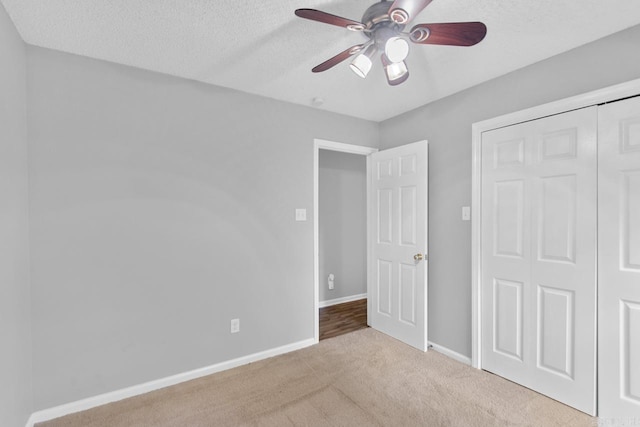 unfurnished bedroom with a textured ceiling, light colored carpet, ceiling fan, and a closet