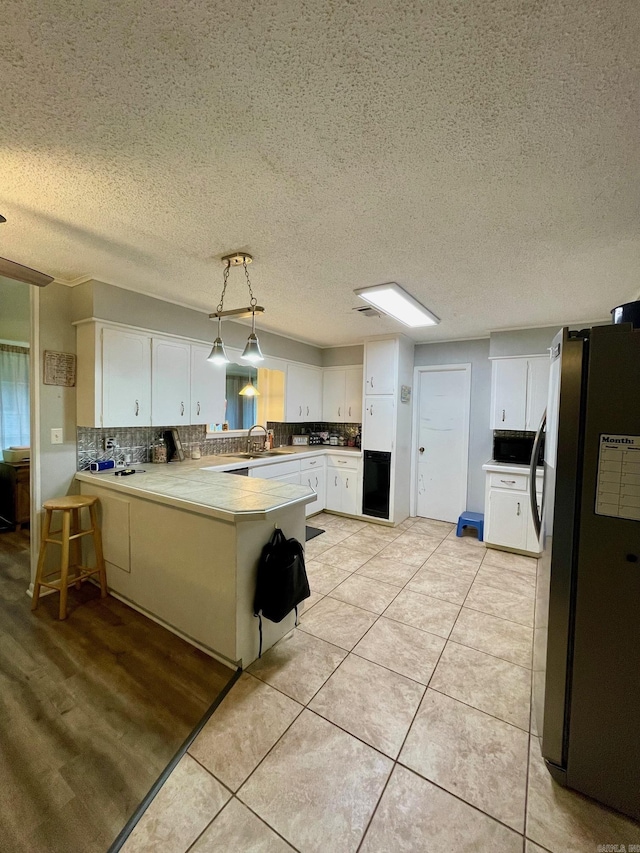 kitchen featuring freestanding refrigerator, a peninsula, a sink, white cabinets, and backsplash