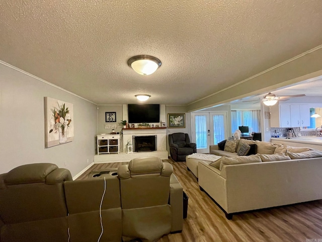living room featuring ornamental molding, a textured ceiling, wood finished floors, a fireplace with raised hearth, and ceiling fan
