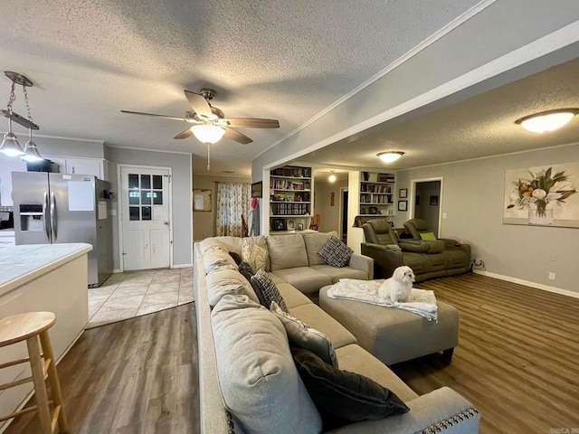 living room featuring a textured ceiling, ceiling fan, baseboards, light wood finished floors, and ornamental molding