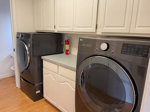 laundry area featuring light wood-type flooring, washer and clothes dryer, and cabinets