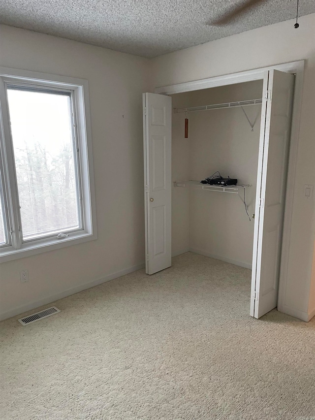 unfurnished bedroom featuring a textured ceiling, light carpet, and a closet