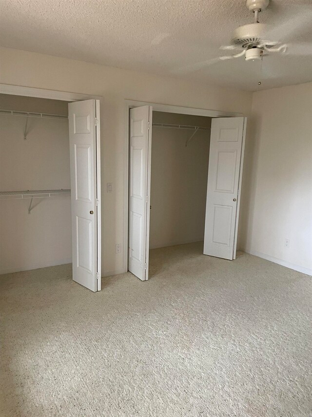 unfurnished bedroom featuring light colored carpet, a textured ceiling, two closets, and ceiling fan