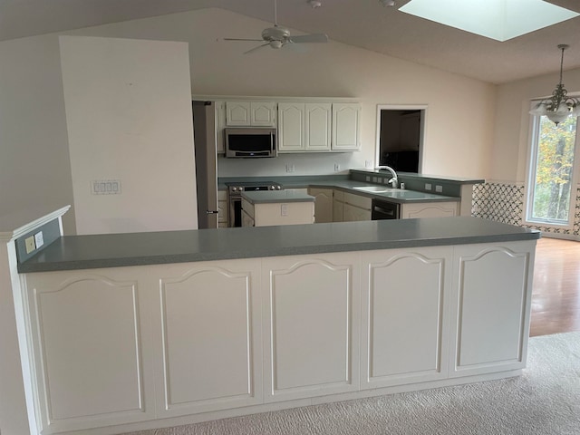 kitchen with vaulted ceiling with skylight, white cabinetry, appliances with stainless steel finishes, kitchen peninsula, and light colored carpet