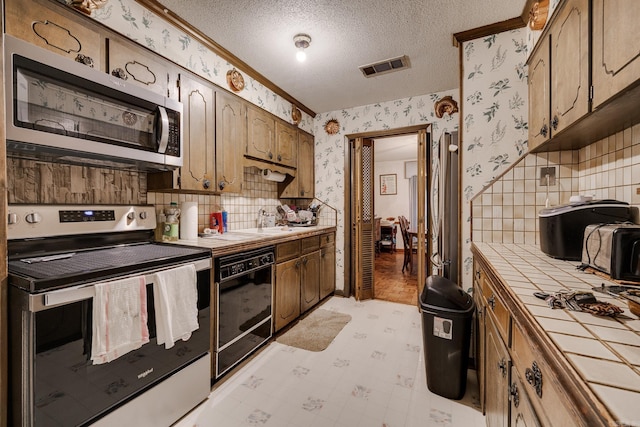 kitchen featuring tasteful backsplash, stainless steel appliances, a textured ceiling, sink, and tile countertops