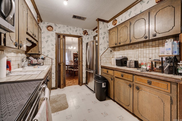 kitchen with stainless steel appliances, tile countertops, a textured ceiling, and a notable chandelier