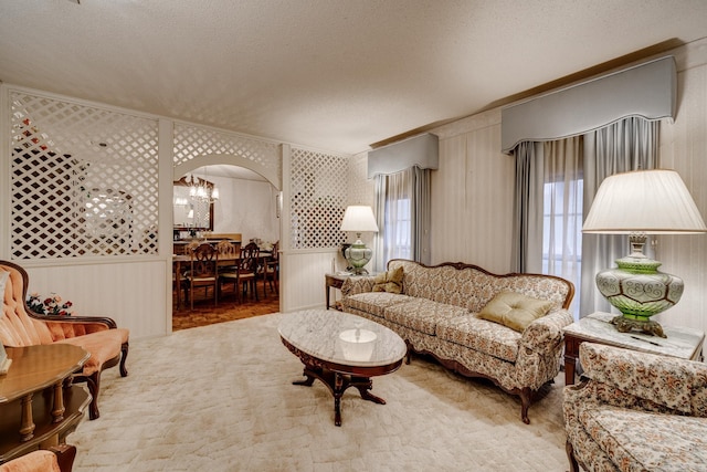 living room with wood walls, a textured ceiling, a notable chandelier, and crown molding