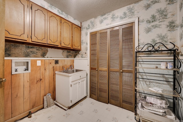 laundry room with cabinets, wood walls, a textured ceiling, sink, and hookup for a washing machine