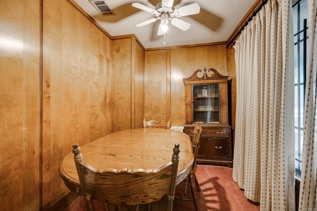 carpeted dining area featuring wood walls, ceiling fan, a textured ceiling, and crown molding