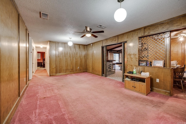 basement featuring wood walls, a textured ceiling, light carpet, and ceiling fan