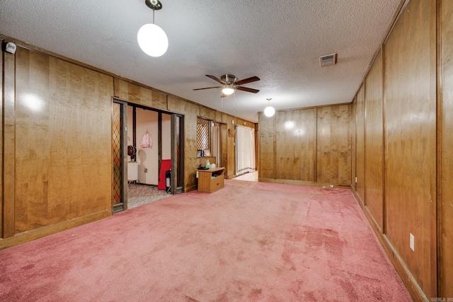 basement featuring a textured ceiling, wood walls, light carpet, and ceiling fan