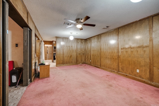 basement featuring wood walls, ceiling fan, a textured ceiling, and carpet