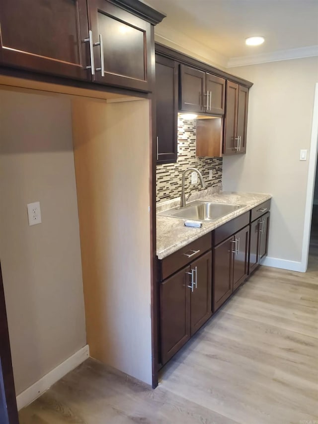 kitchen featuring backsplash, dark brown cabinetry, crown molding, sink, and light hardwood / wood-style flooring