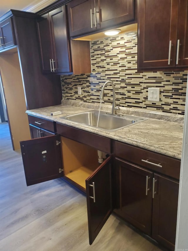 kitchen featuring light stone countertops, sink, decorative backsplash, dark brown cabinets, and light wood-type flooring