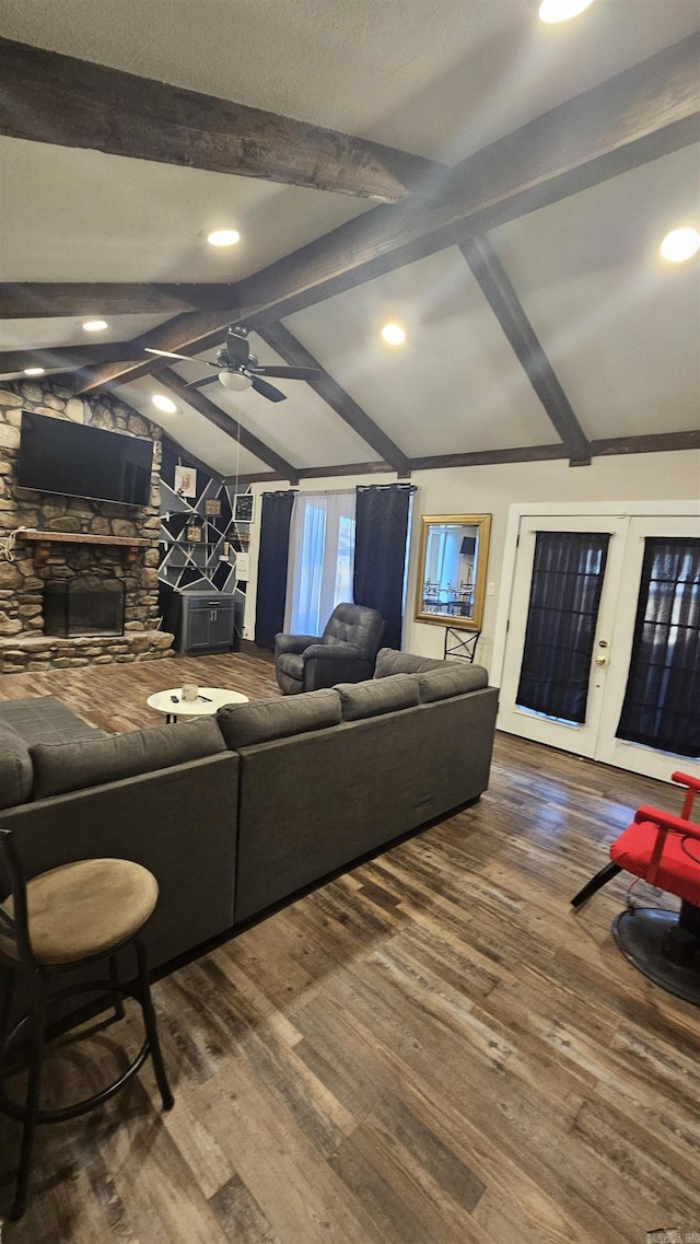 living room featuring vaulted ceiling with beams, ceiling fan, a stone fireplace, and wood finished floors