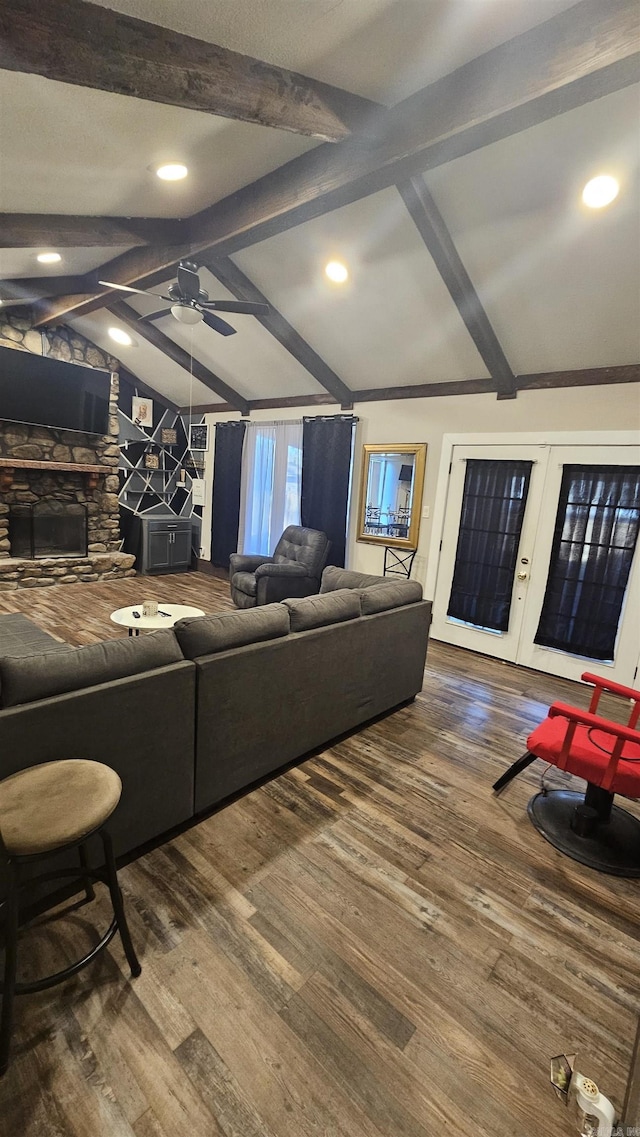 living area featuring ceiling fan, wood finished floors, a stone fireplace, vaulted ceiling with beams, and french doors