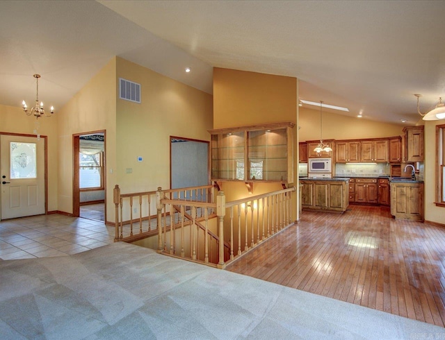 kitchen with hanging light fixtures, sink, white microwave, and light hardwood / wood-style flooring