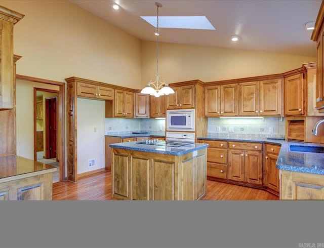 kitchen featuring white appliances, decorative backsplash, sink, a skylight, and light hardwood / wood-style flooring