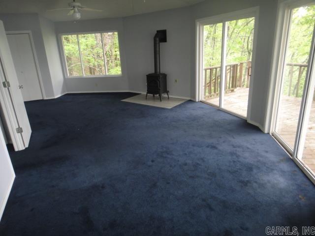 85 Bluff View Dr, Quitman, AR 72131 - unfurnished living room featuring a wood stove, a ceiling fan, dark carpet, and plenty of natural light