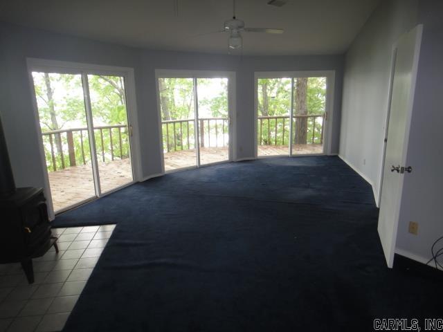 85 Bluff View Dr, Quitman, AR 72131 - unfurnished living room featuring carpet floors, a ceiling fan, a wood stove, and baseboards
