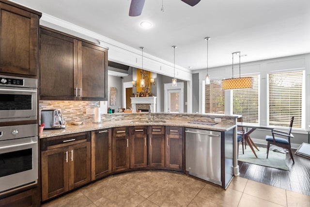 kitchen featuring stainless steel appliances, sink, light stone counters, ceiling fan, and decorative light fixtures