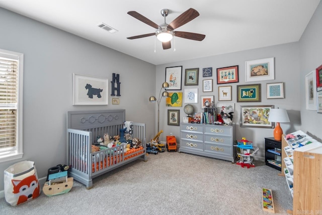 carpeted bedroom with multiple windows, ceiling fan, and a crib