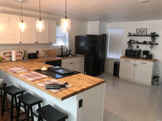 kitchen with kitchen peninsula, black appliances, a breakfast bar area, butcher block countertops, and white cabinetry