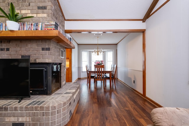 dining area featuring dark hardwood / wood-style flooring, a textured ceiling, a chandelier, ornamental molding, and a fireplace