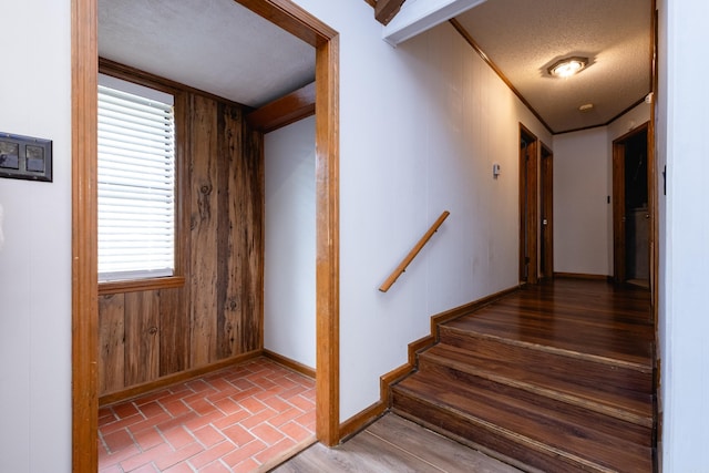 stairs with wooden walls, a textured ceiling, and crown molding