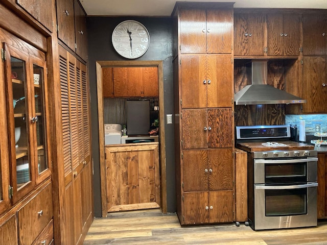 kitchen with light wood-type flooring, wall chimney range hood, stainless steel gas stove, and washer / clothes dryer