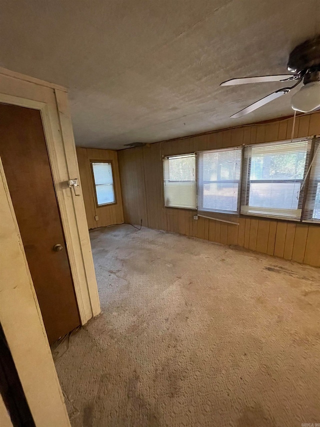 empty room featuring wooden walls, light carpet, and ceiling fan