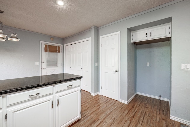 kitchen with a textured ceiling, light hardwood / wood-style flooring, white cabinetry, and dark stone countertops