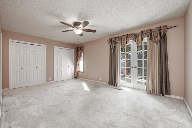 unfurnished bedroom with ceiling fan, french doors, light colored carpet, a textured ceiling, and two closets