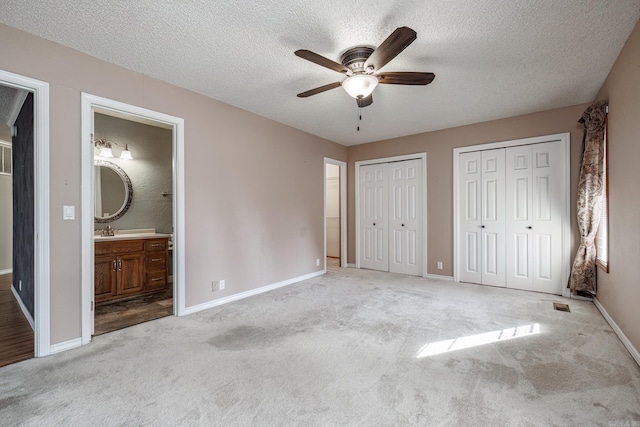 unfurnished bedroom with light carpet, a textured ceiling, ceiling fan, sink, and connected bathroom