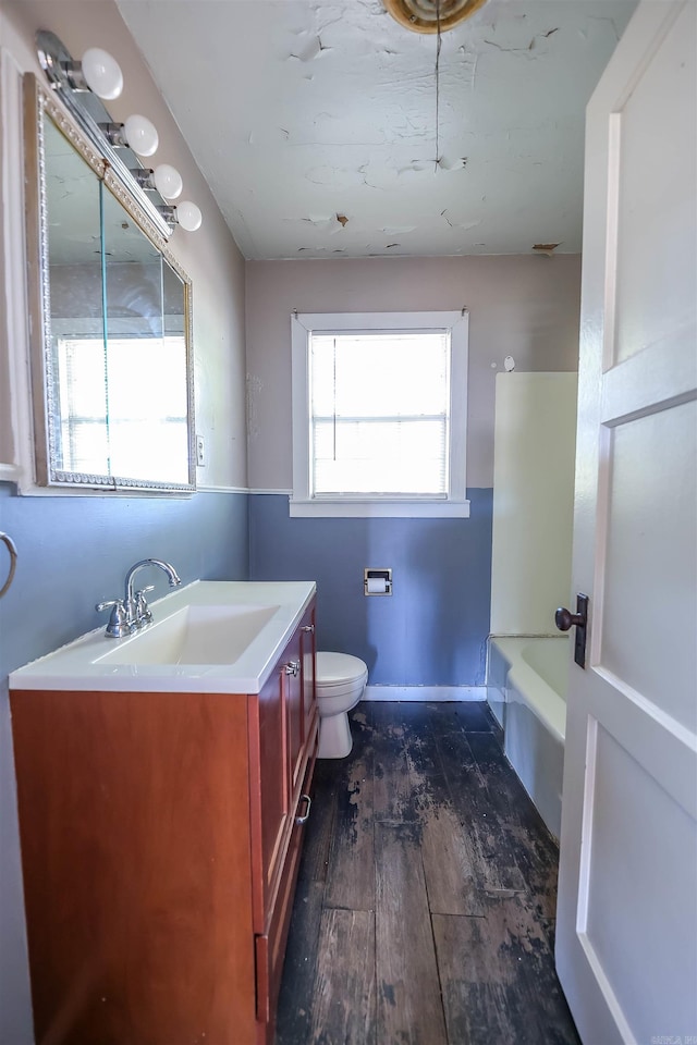 bathroom with hardwood / wood-style floors, a tub to relax in, vanity, and toilet