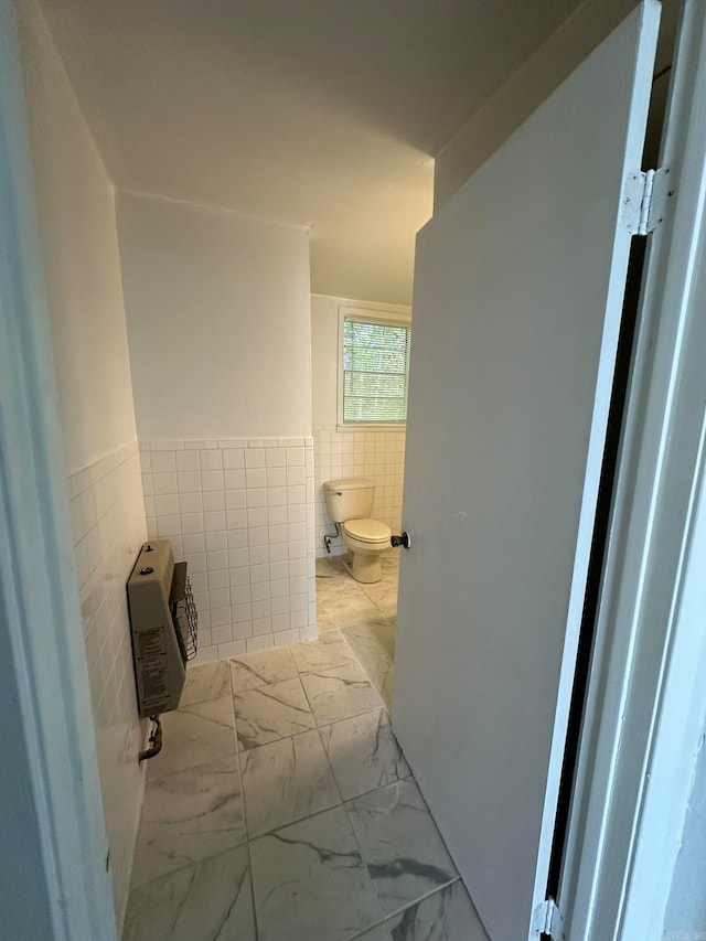 bathroom featuring heating unit, toilet, and tile walls